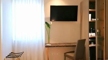 A hotel room with a bed, a desk with a chair, a television mounted on the wall, and a cabinet with shelves.