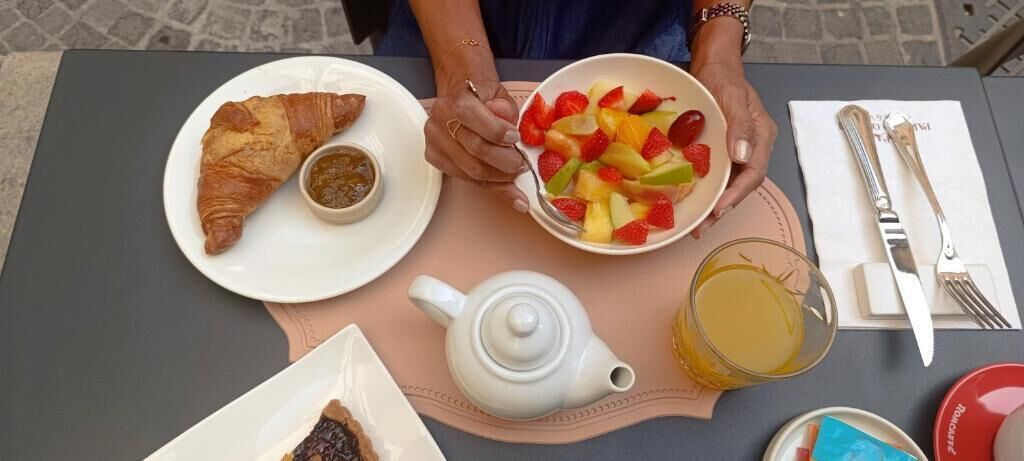 A table with a croissant, fruit bowl, teapot, and a glass of juice.