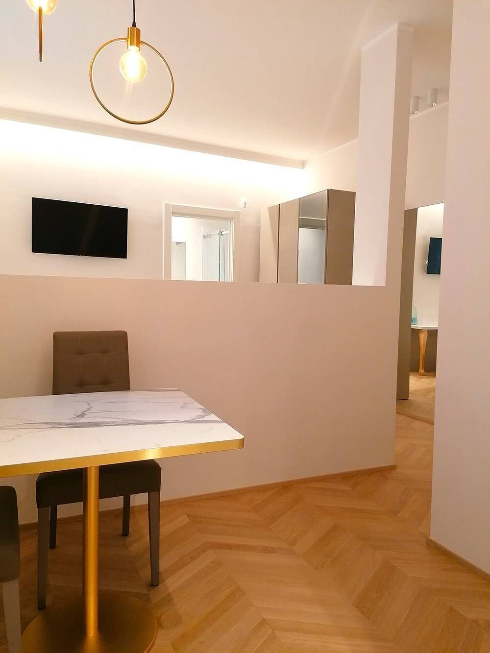A modern interior with a dining table, chairs, a television, and a wooden herringbone floor.