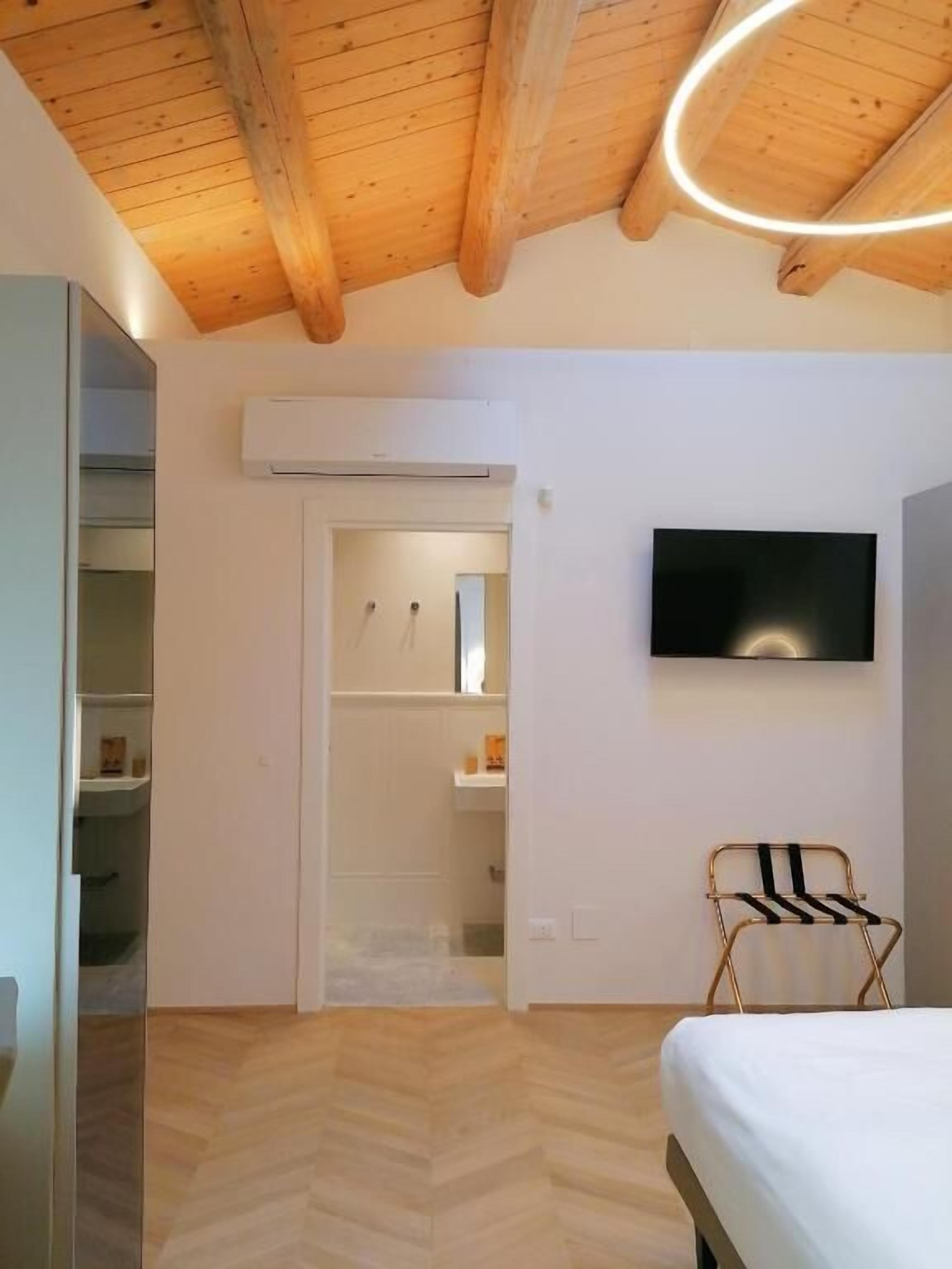 A bedroom with a bed, a TV mounted on the wall, a wooden ceiling, and a closet with a mirror.