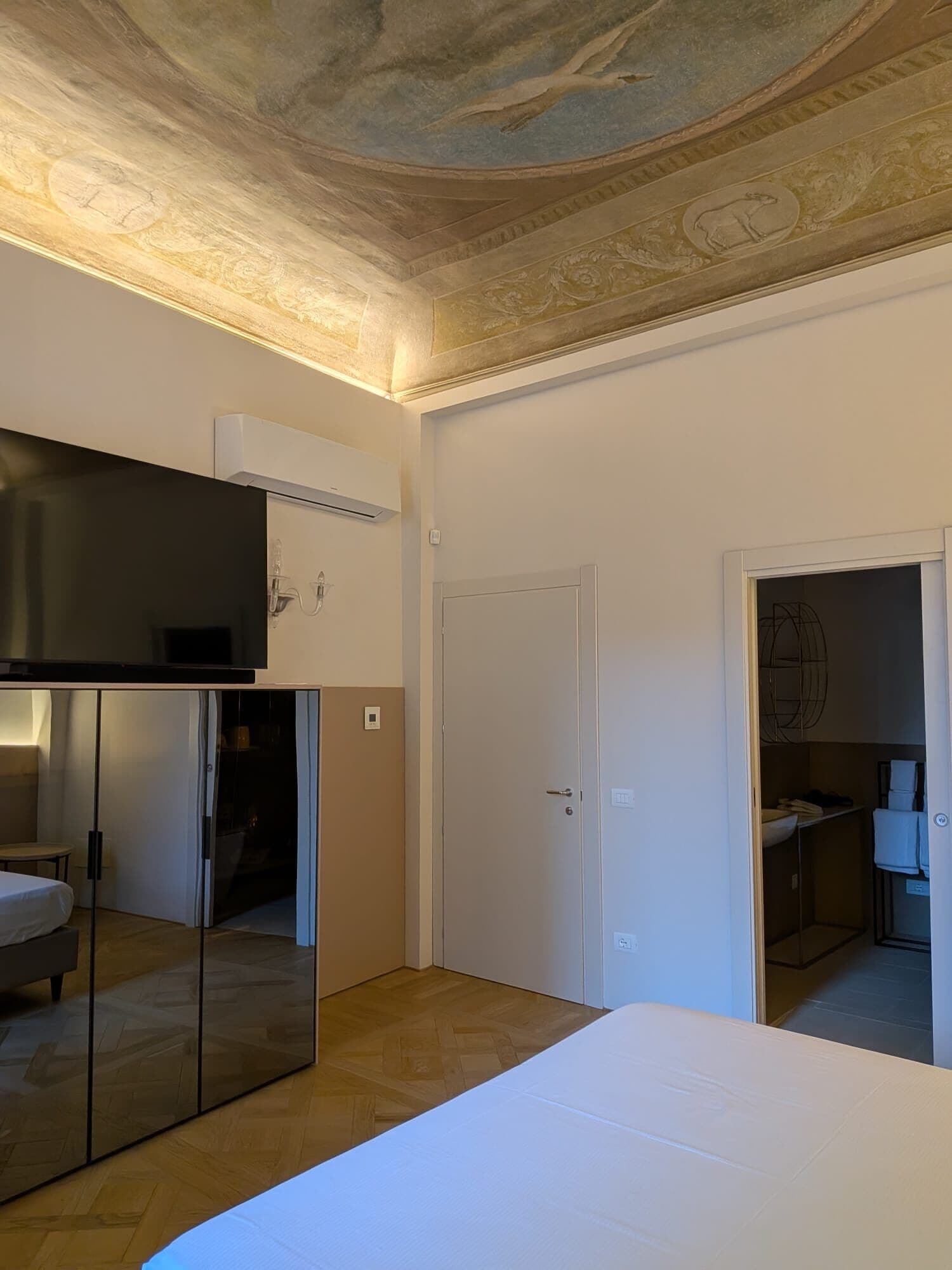 Un dormitorio con cama, armario, espejo y techo con detalles decorativos.
