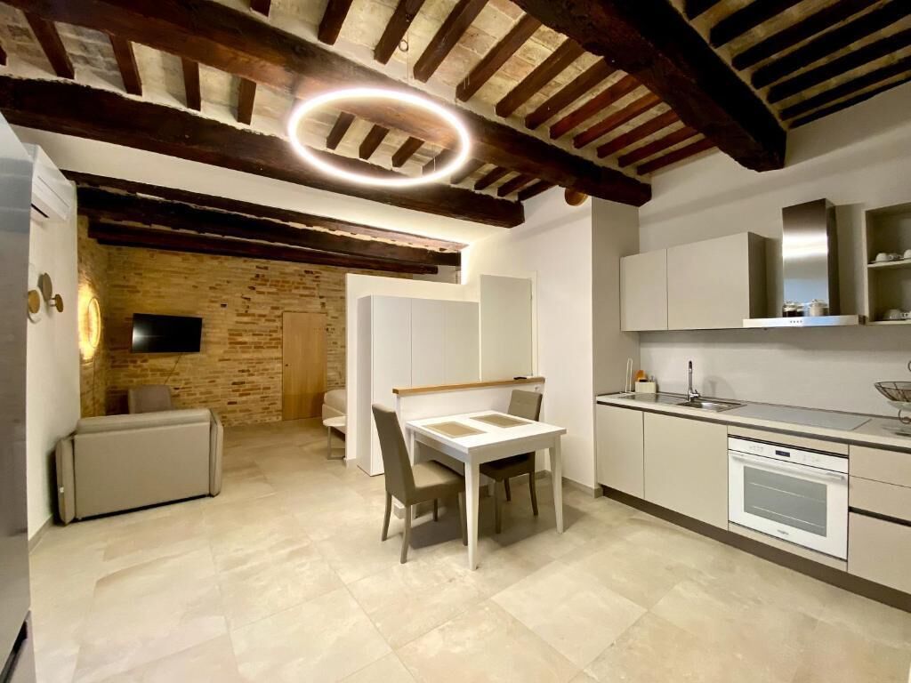 A modern kitchen with a built-in oven, a dining area with a table and chairs, and a brick wall in the background.