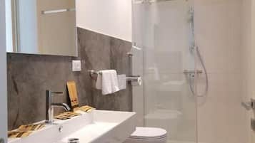 A modern bathroom with a glass-enclosed shower, a white sink, and a toilet.