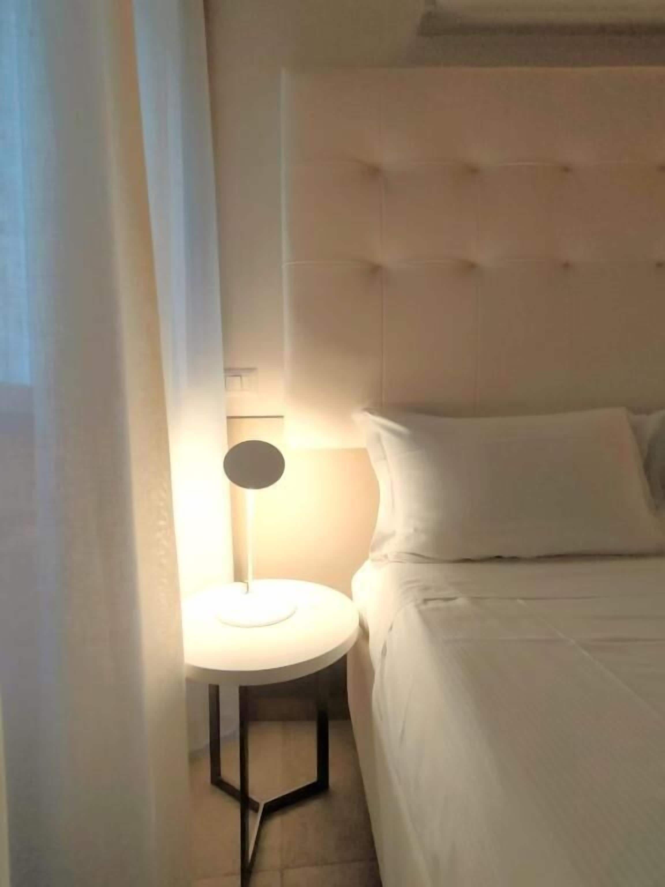 Un dormitorio con cama, una mesita de noche con lámpara y una ventana con cortinas.