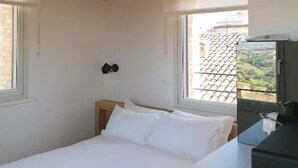 Un dormitorio con cama, mesita de noche, ventana y vistas al exterior.