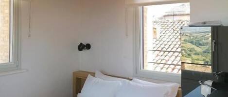 Un dormitorio con cama, mesita de noche, ventana y vistas al exterior.