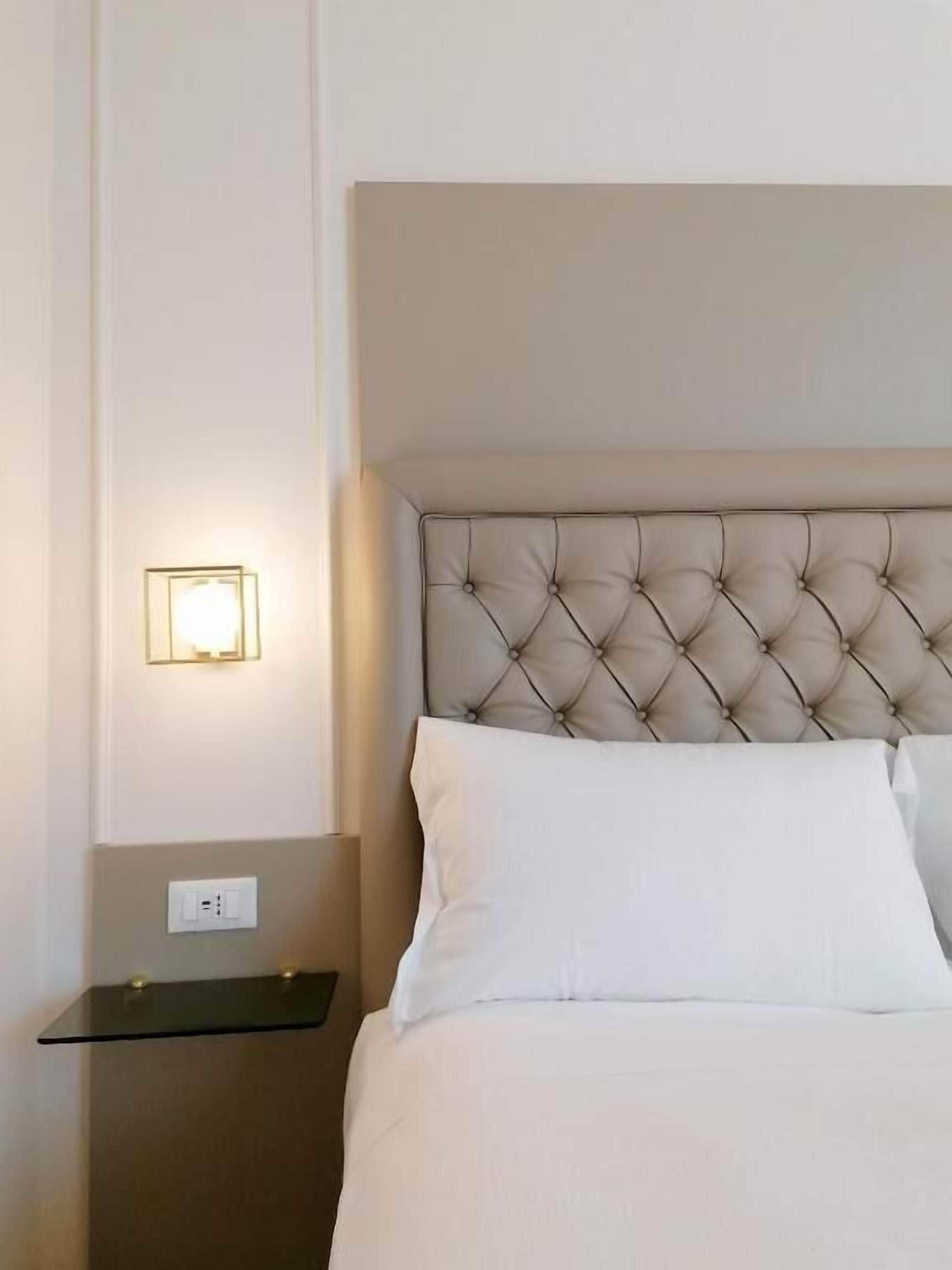 Ein Hotelzimmer mit einer gepolsterten Kopfteil, einem Nachttisch und einer Wandleuchte.