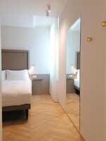 A hotel room with a bed, bedside table, and a mirror.