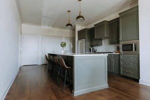 A modern kitchen with a central island, bar stools, stainless steel appliances, and dark cabinetry.