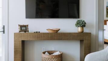A living room with a flat-screen TV mounted above a wooden console table, a woven basket, and a white sofa.
