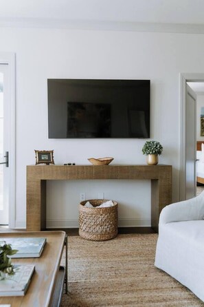 A living room with a flat-screen TV mounted above a wooden console table, a woven basket, and a white sofa. - Lovely 2BR · Williams-Brice & Fort Jackson (Columbia)