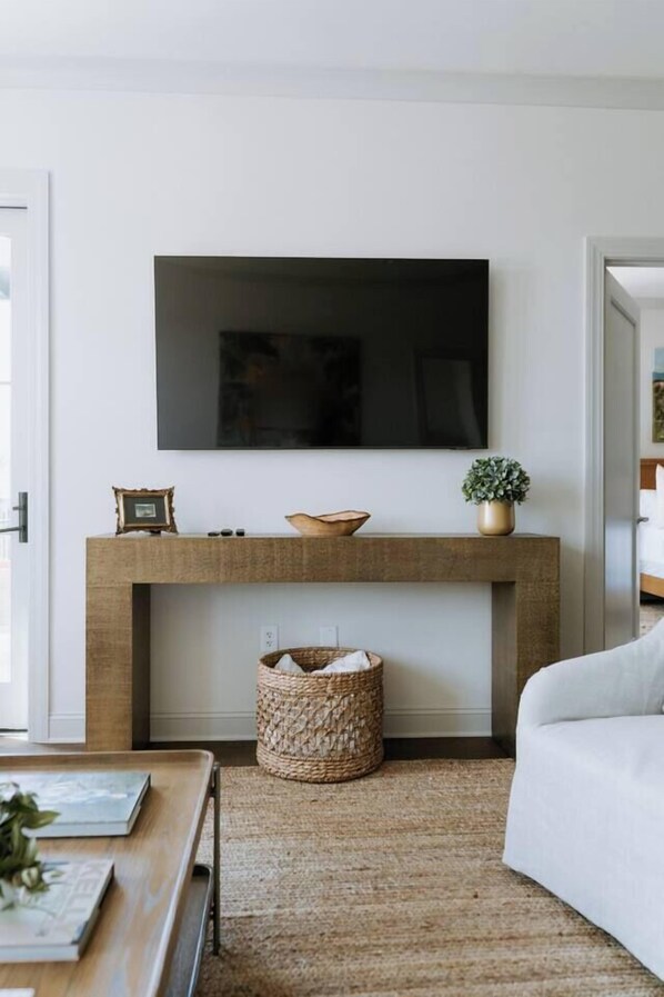 A living room with a flat-screen TV mounted above a wooden console table, a woven basket, and a white sofa.
