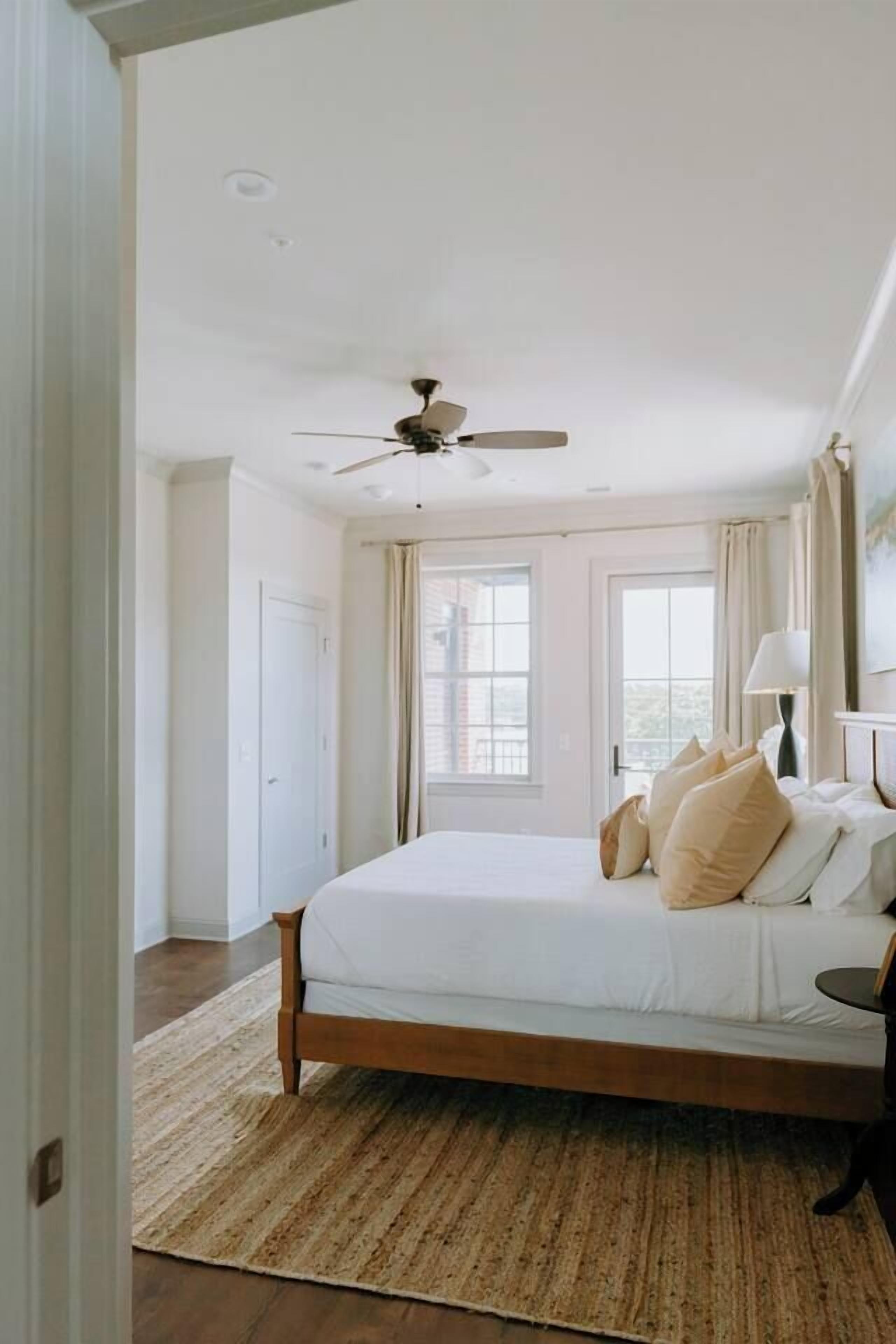 A bedroom with a bed, a ceiling fan, a window, and a door.