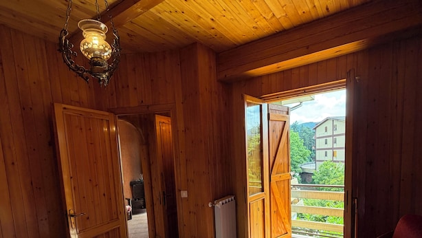 A wooden room with a bed, a hanging light fixture, and a view of the outside. - Cozy mountain apartment (Altipiani di Arcinazzo)