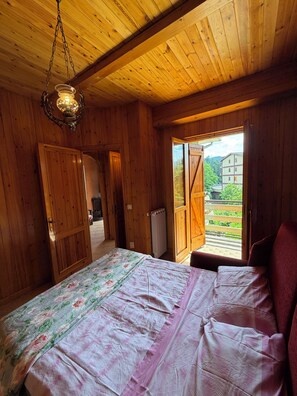 Ein Zimmer mit Holzboden, einem Bett, einer Hängelampe und Blick ins Freie.