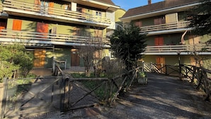A courtyard with a gravel path, wooden fences, and buildings with balconies and windows. - Cozy mountain apartment (Altipiani di Arcinazzo)