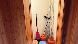 A wooden-paneled room with a door leading to a storage area containing cleaning equipment and gas cylinders. - Cozy mountain apartment (Altipiani di Arcinazzo)