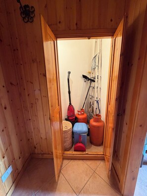 A wooden-paneled room with a door leading to a storage area containing cleaning equipment and gas cylinders. - Cozy mountain apartment (Altipiani di Arcinazzo)