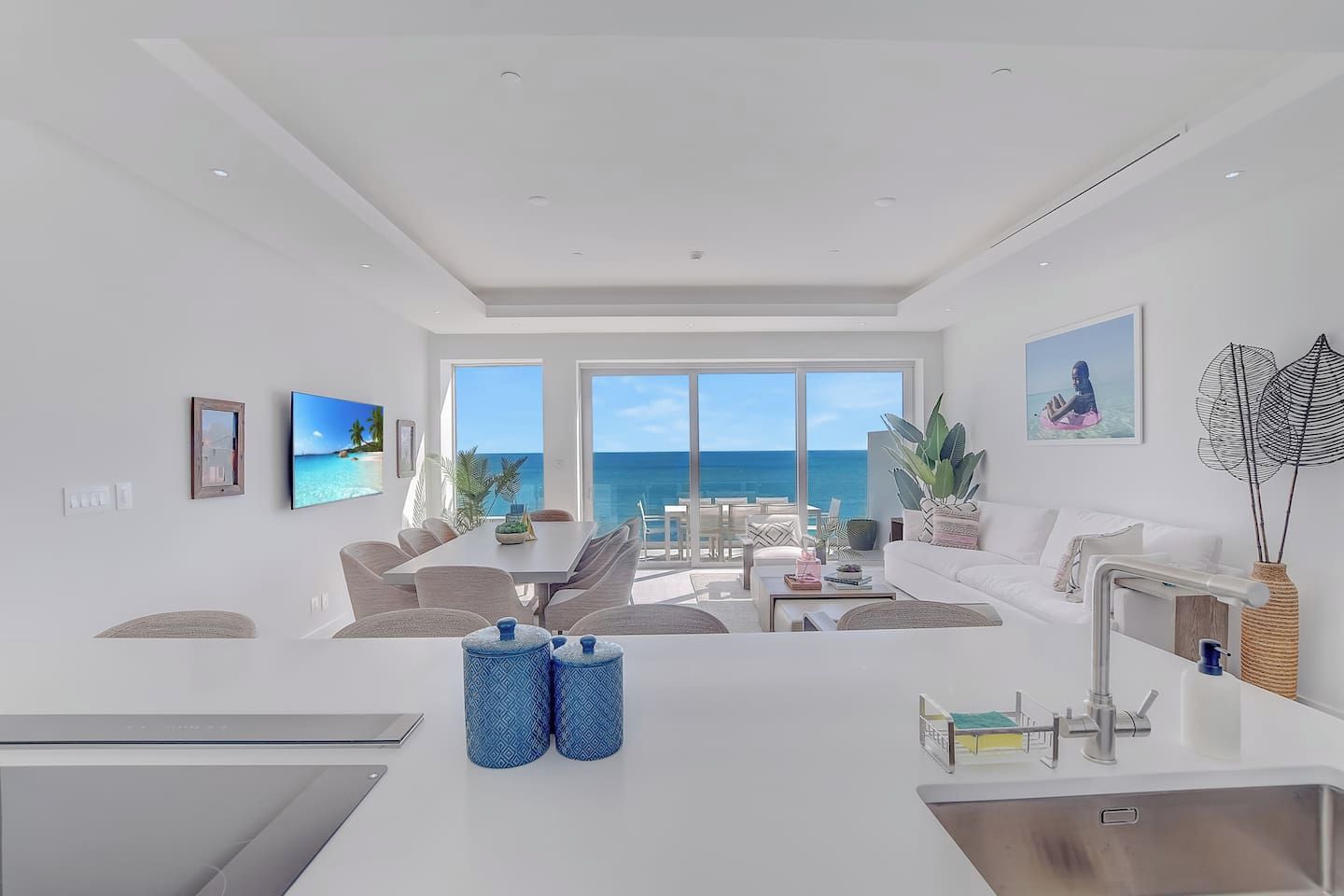 Un salon moderne doté d’une grande fenêtre donnant sur la mer, un coin repas avec vue et une cuisine équipée d’un évier et d’un plan de travail.