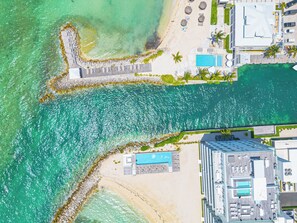 An aerial view of a coastal hotel with a swimming pool, beach area, and a rocky shoreline.