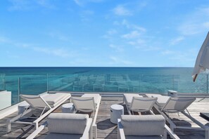 A deck with lounge chairs and a glass barrier overlooking a clear blue sea.
