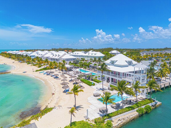 A resort with multiple white buildings, a beach, a pool area, and palm trees.