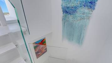 A modern interior with glass shelving, a hanging artwork, and a framed picture.
