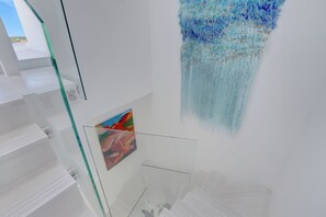 A modern interior with glass shelving, a hanging artwork, and a framed picture. - Palm Cay - 3BR Beachfront Penthouse + Private Pool (Nassau)