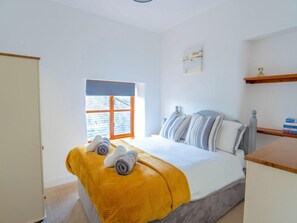 Ein Schlafzimmer mit Bett, Fenster, Nachttisch und Ablagefläche.