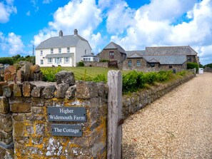 Eine Steinsäule mit Schildern, auf denen 'Higher Widemouth Farm' und 'The Cottage' stehen.