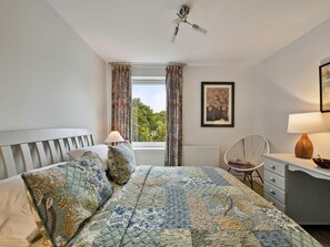 A bedroom with a bed, a chair, a desk, a window with curtains, a ceiling fan, and a framed picture on the wall. - Stylish Apartment by Loch Lomond (Alexandria)