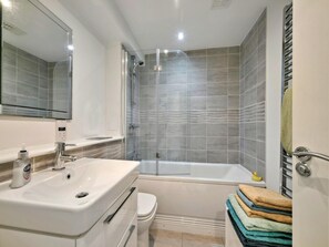 A modern bathroom with a glass-enclosed shower, a bathtub, and a sink with a soap dispenser. - Stylish Apartment by Loch Lomond (Alexandria)