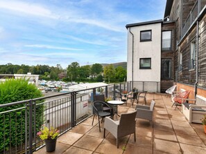 A balcony with outdoor furniture, a view of a marina, and a building with a modern design. - Stylish Apartment by Loch Lomond (Alexandria)
