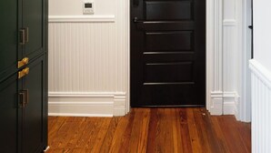 Une pièce avec une porte en bois foncé, des lambris blancs et un thermostat fixé au mur.