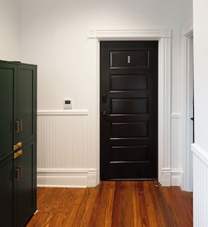 Una habitación con una puerta de madera oscura, paneles de madera blancos y un termostato en la pared.