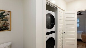 Une buanderie avec deux machines à laver, une porte blanche et un tableau accroché au mur.