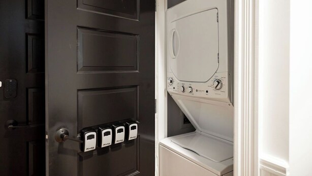 Une porte dotée d’une serrure de sécurité et d’un clavier, ainsi qu’un appareil électroménager blanc, peut-être un lave-linge et un sèche-linge, dans une pièce.
