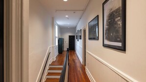 Un couloir doté d’un plancher en bois, de murs blancs et de tableaux encadrés sur le côté droit.
