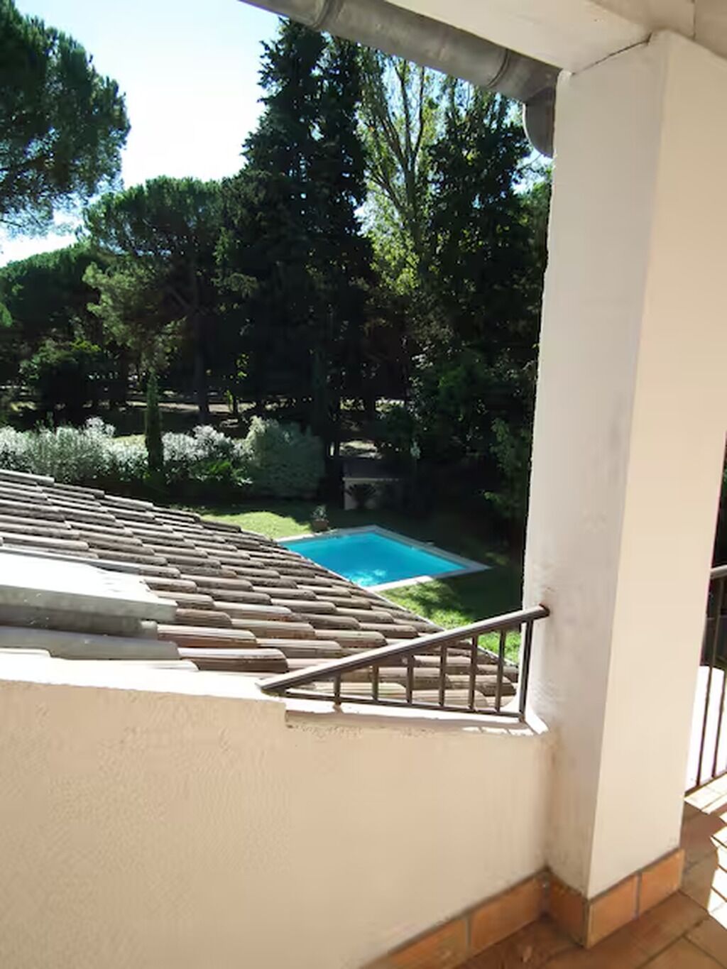 En balkon med udsigt over en swimmingpool omgivet af træer.