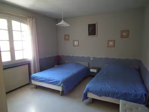 Un dormitorio con dos camas, un radiador, una ventana con cortinas y una pared con cuadros.