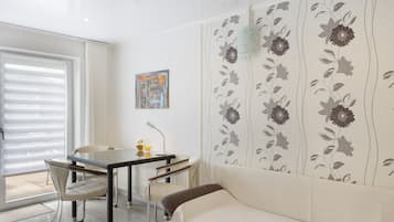 A room with a sofa, a table with chairs, a window with blinds, and a wall with floral wallpaper.