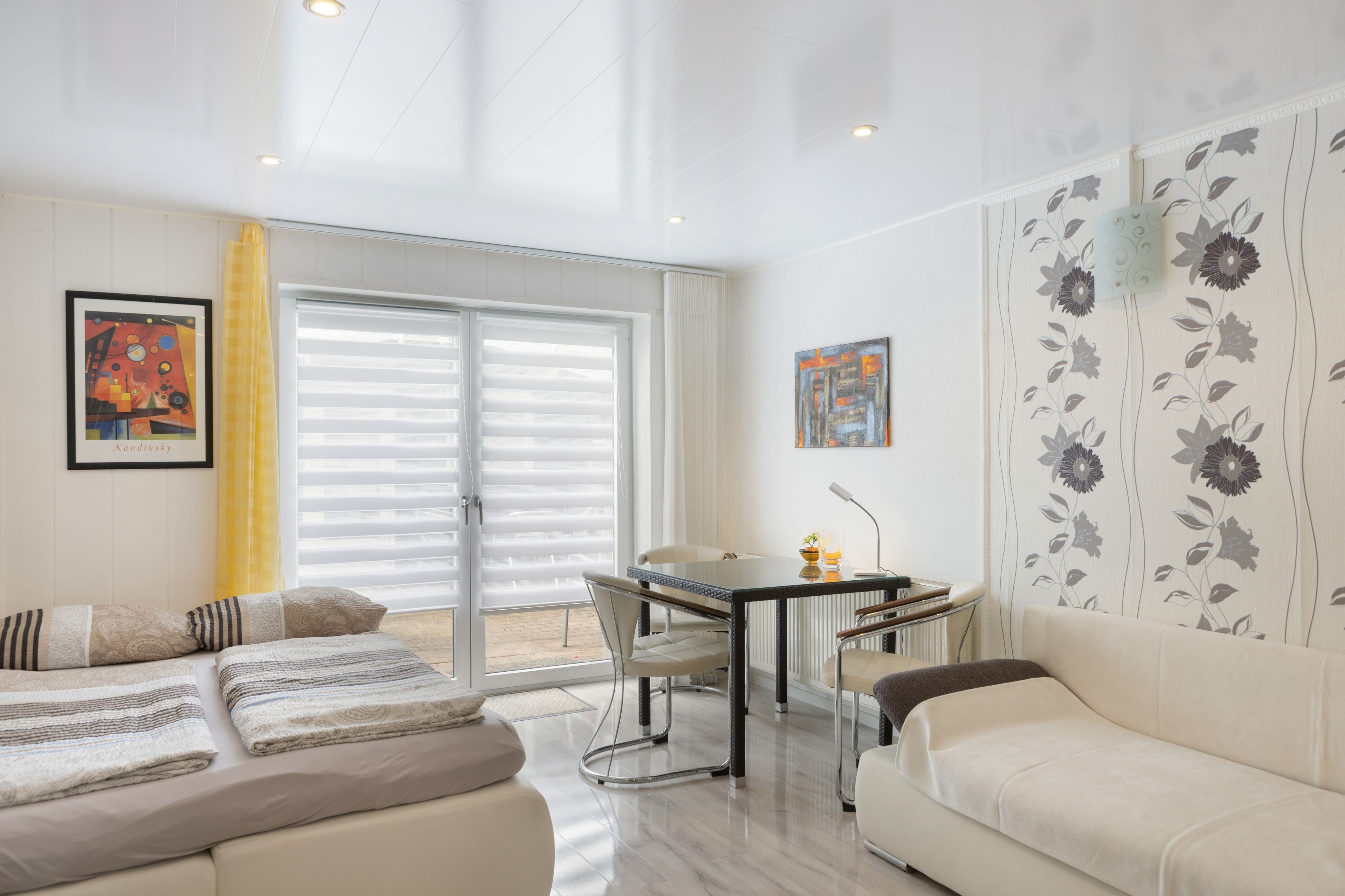 Ein modernes Wohnzimmer mit einer Couch, einem Esstisch mit Stühlen und einem großen Fenster mit Jalousien.