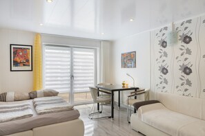 A modern living room with a sofa, a dining table with chairs, and a large window with blinds. - Holiday Apartment in Rotkäppchenland with Terrace and Wi-Fi (Schwalmstadt)
