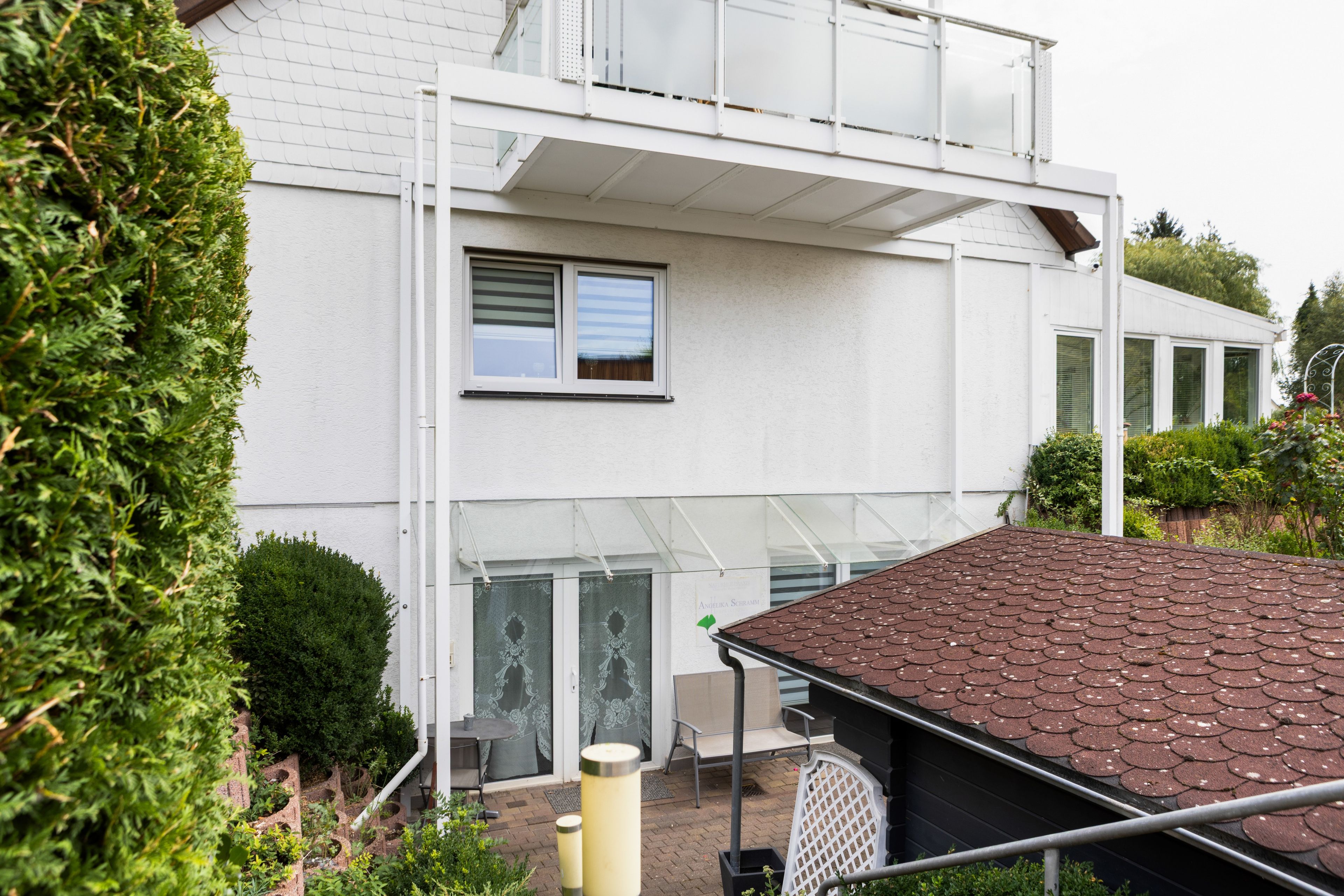 Ein modernes, zweistöckiges Haus mit Flachdach, Balkon und einem Fenster mit Rollläden.