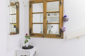 Et værelse med hvid væg, et vindue med træramme, et lille bord dækket med et hvidt stof og en potteplante.