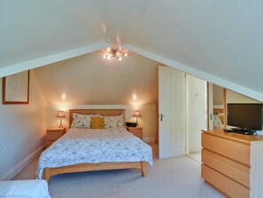 A bedroom with a sloped ceiling, a bed with floral bedding, bedside lamps, a dresser, and a television. - Apartment With Jacuzzi Bath (Torpoint)