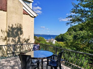 A balcony with a round table and chairs, overlooking a coastal view with trees and buildings. - Apartment With Jacuzzi Bath (Torpoint)