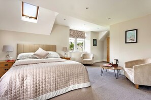 A bedroom with a large bed, a sitting area with a chair, a small table, and a window with a view. - Cozy Stay Near the Fells (Ambleside)