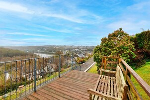 Una terraza de madera con barandilla metálica que da vista a una zona residencial y un río.