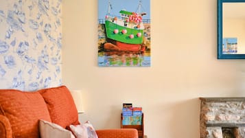 A room with a painting of a boat, a sofa, a lamp, and a fireplace.